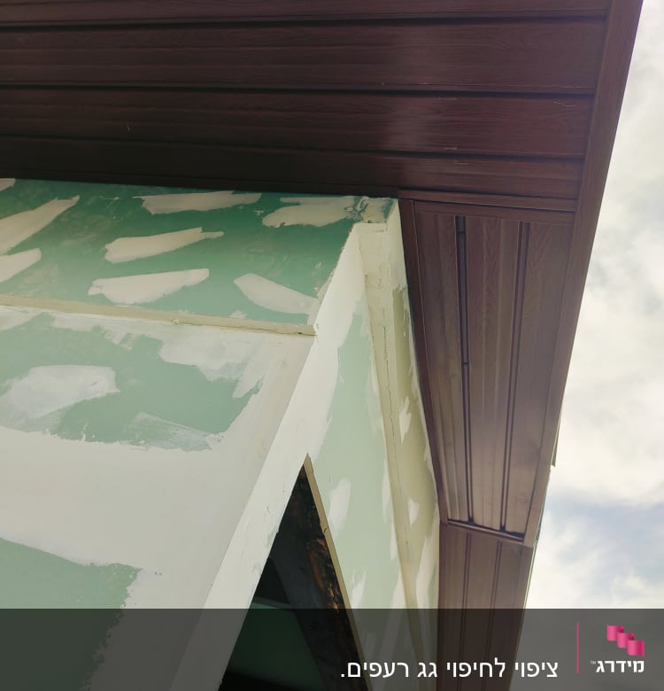 גג עץ חום מעל קיר ירוק עם טיח לבן